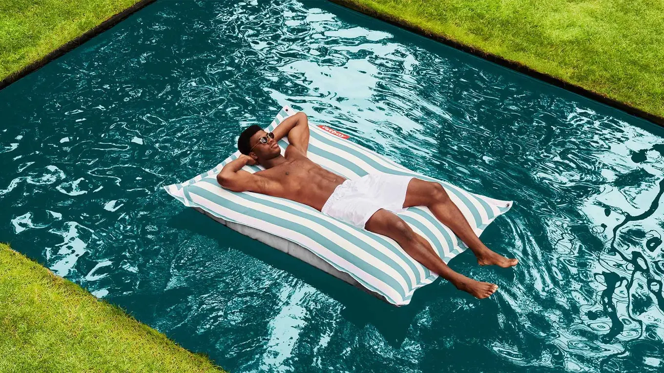 Mann liegt auf einem Fatboy Original Floatzac Sitzsack in hellblau streifen im pool