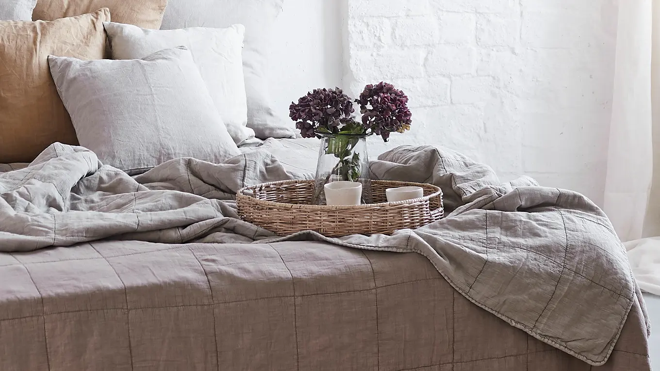 Rattantablett mit frischen hortensien steht auf einem sika design bett mit tagesdecke